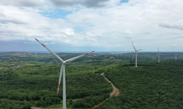 A wind turbine above green forest with turbines on the far ridges
