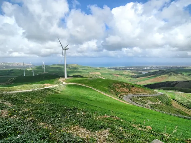 A wind turbine on green hills with a road curving below