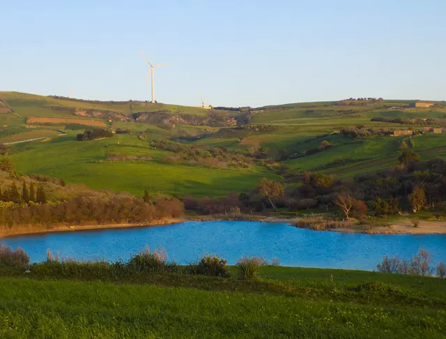 Wind turbines on green hills above a blue lake