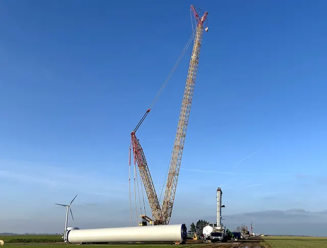 A tall crane assembling a wind turbine beside its tower sections
