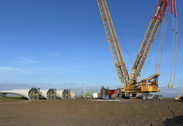 Two crane booms over turbine blades laid out on site