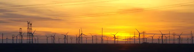 Wind turbines and pylons in silhouette against an orange desert sunset