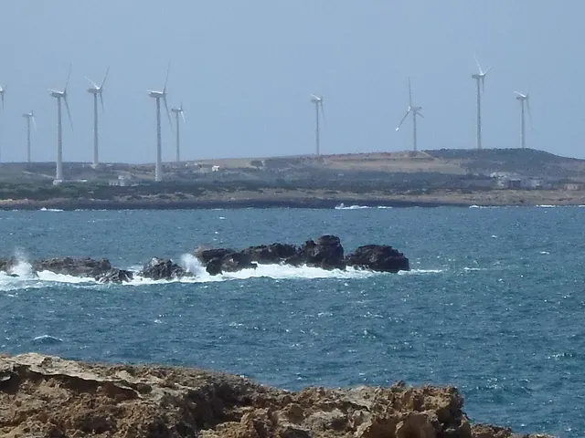 Wind turbines on a low headland beyond waves breaking on rocks