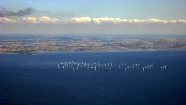 An offshore wind farm seen from the air beneath a coastline