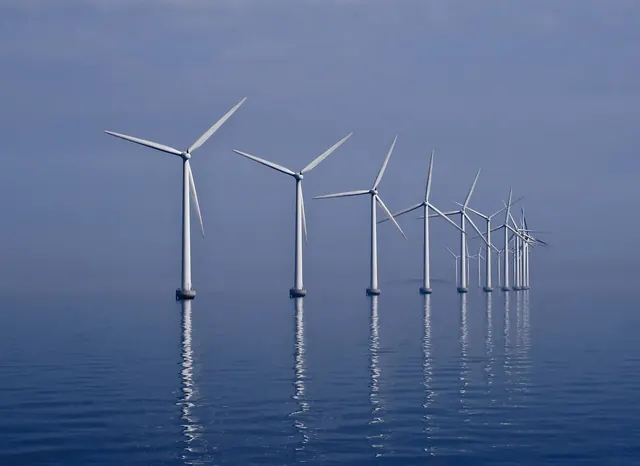 A curved line of offshore wind turbines reflected in calm water