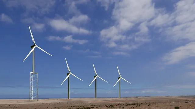 A row of wind turbines and a lattice tower under a cloudy sky