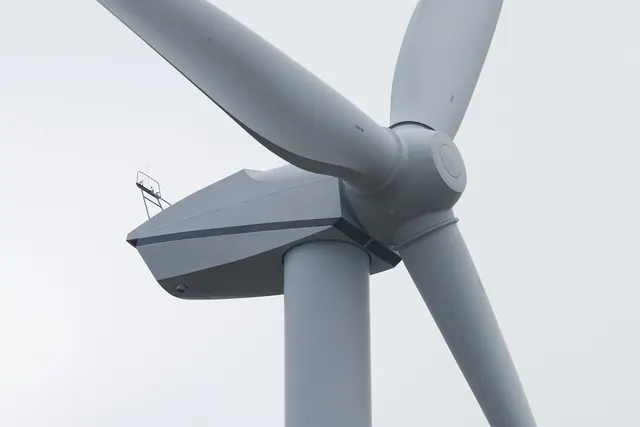 The nacelle and rotor of a wind turbine against a white sky