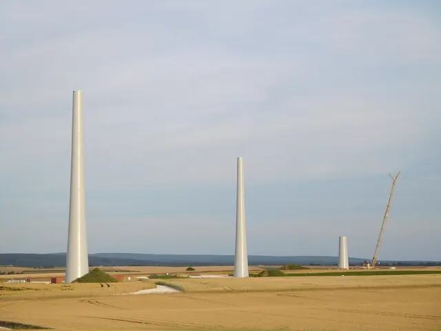 Bare turbine towers rising from farmland with a crane nearby