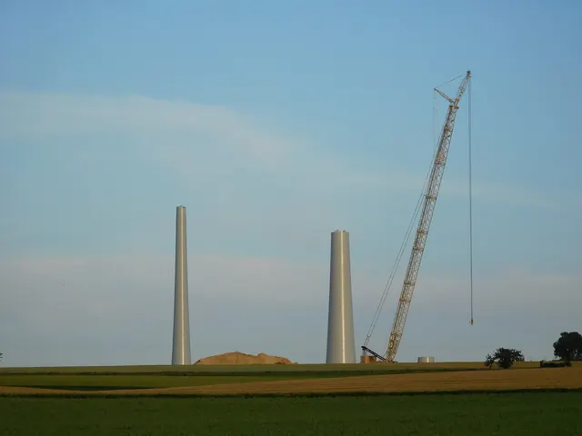 Two turbine towers and a crane on a wide plain