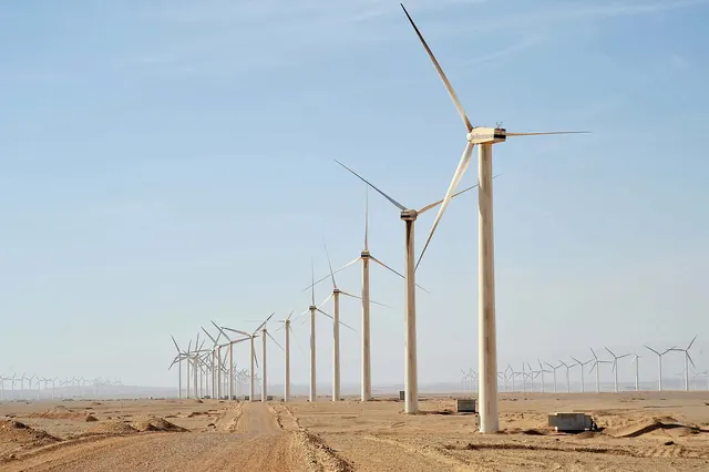 Wind turbines lining a sandy road toward the horizon