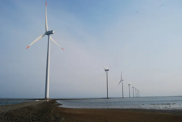 Wind turbines on a shoreline beneath a hazy sky