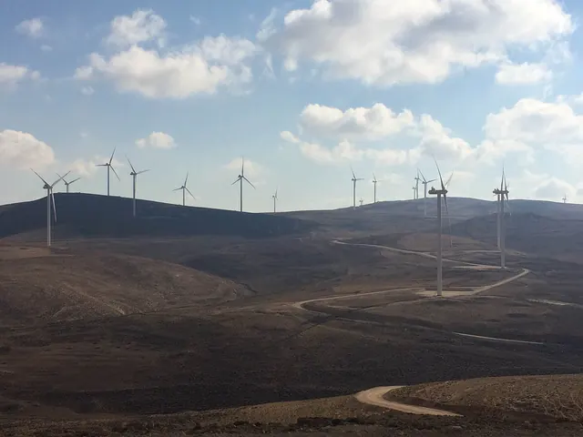 Wind turbines along dark ridges with a winding road at Tafila