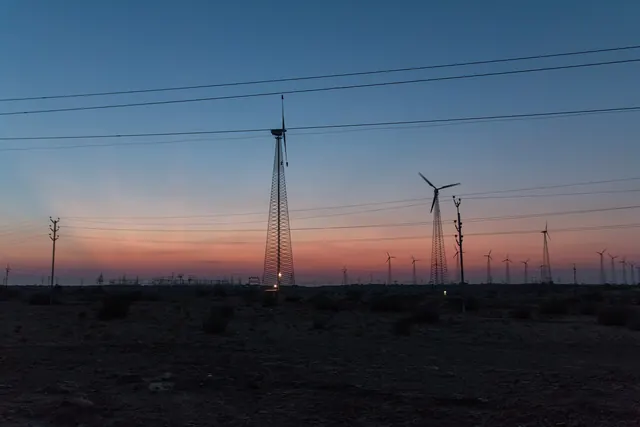 Wind turbines and power lines against an orange dawn sky