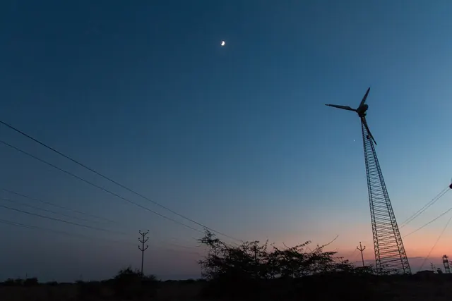 A lattice wind turbine and power lines at twilight