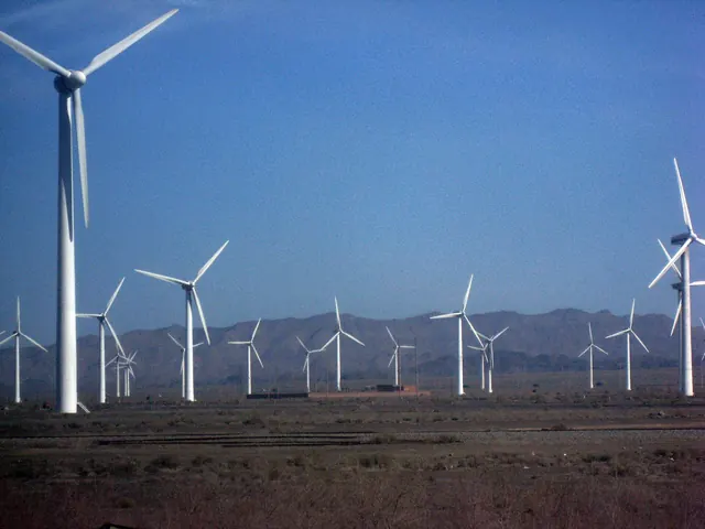 Rows of wind turbines on a desert plain beneath mountains