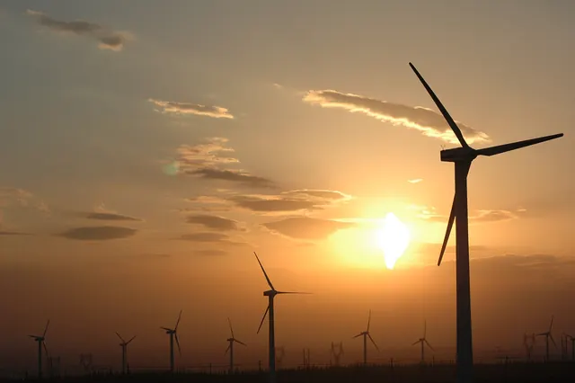 A wind turbine in silhouette against the setting sun