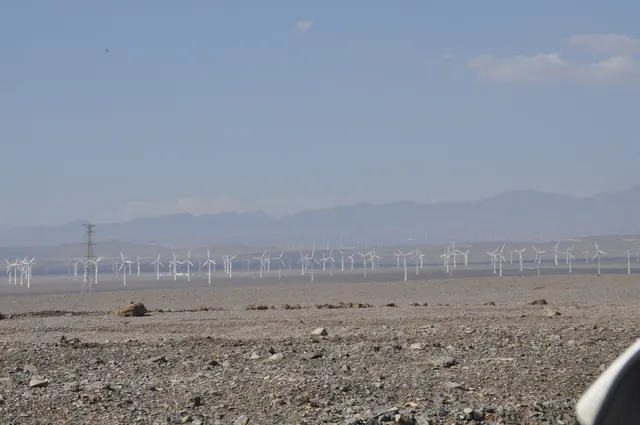 Rows of wind turbines on a gravel plain below mountains