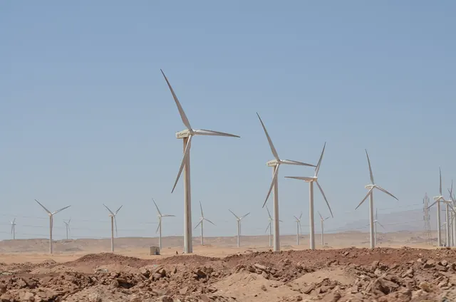 Wind turbines on a pale desert plain with mountains in the haze