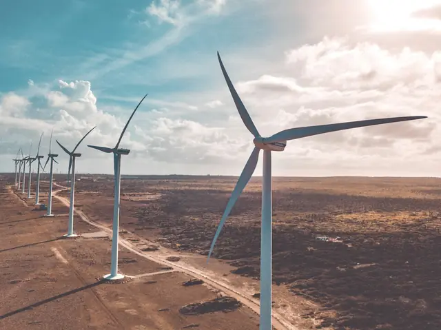 A row of wind turbines along a dirt track across dry, open land
