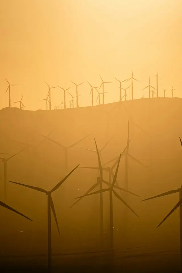 Wind turbines in silhouette on a hazy ridge at sunset