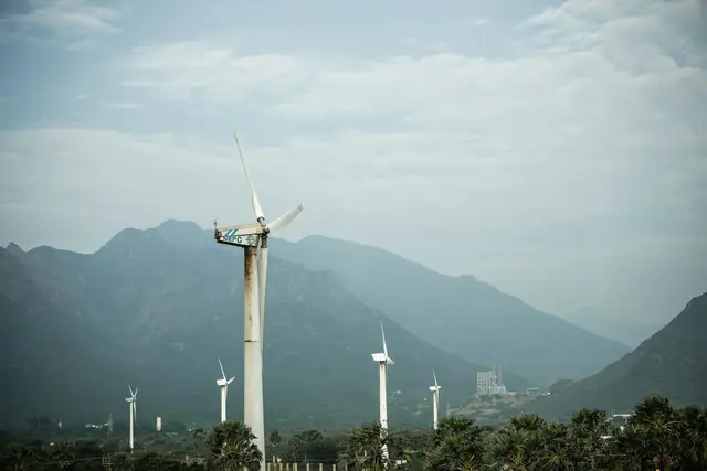 Wind turbines on a green valley floor beneath misty mountains
