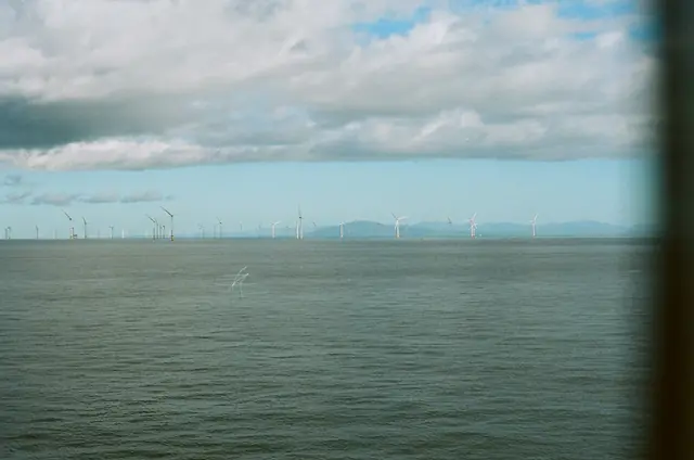 A distant offshore wind farm seen across grey-green water