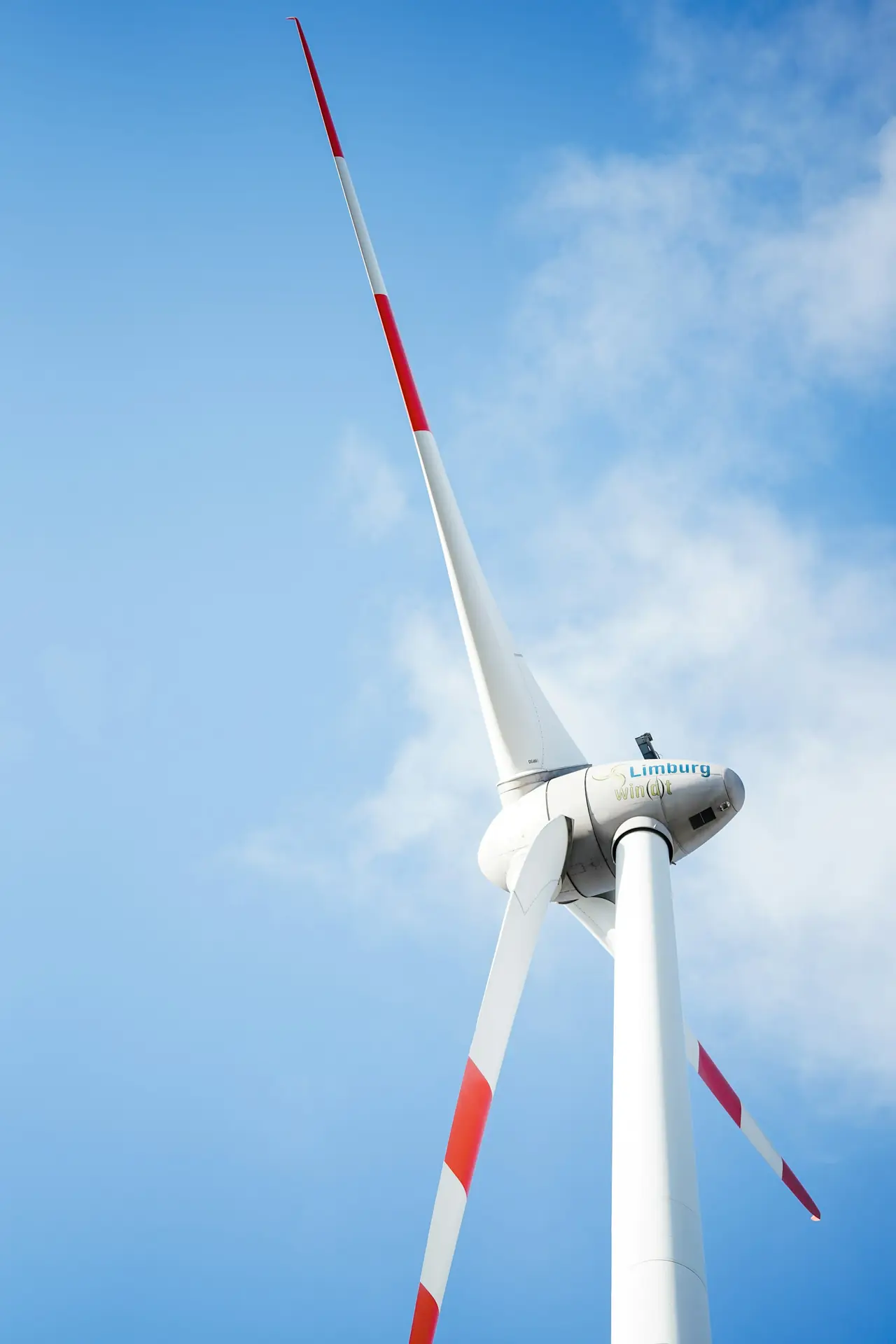 A red and white turbine against a bright sky, seen from below